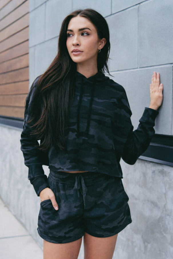 Woman wearing a black camouflage outfit against a gray wall.