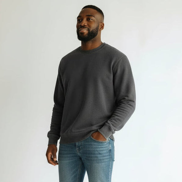 Man wearing a dark gray sweater and blue jeans standing against a white background