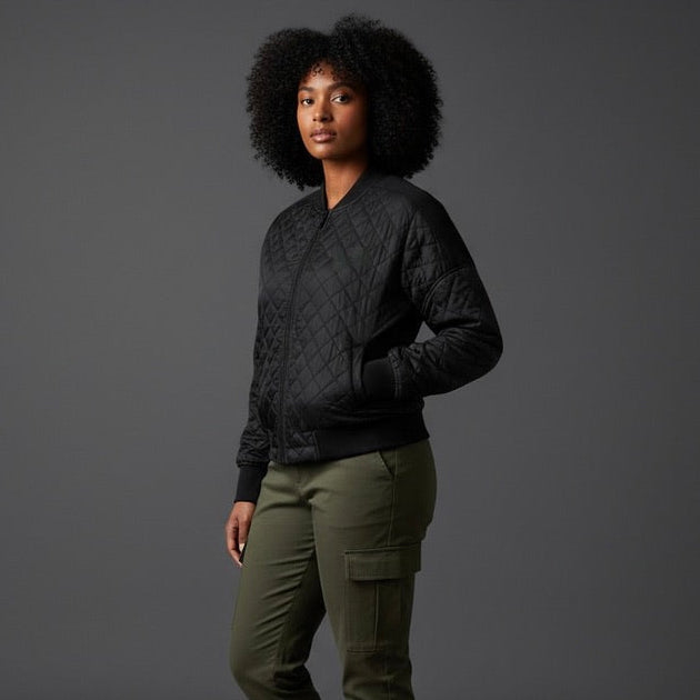Woman wearing a dark quilted jacket, green cargo pants, and black boots against a gray background